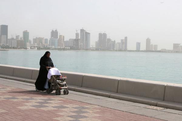 Mulher com roupa típica caminhando com bebê pelo corniche
