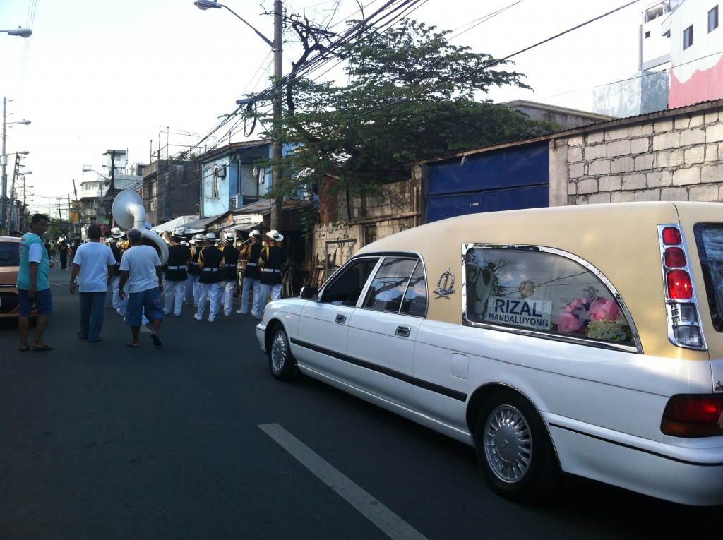 Carro fúnebre acompanhado pela banda é quem puxa o cortejo.